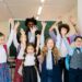 Joyful group of diverse school children raising their hands in an indoor classroom setting.