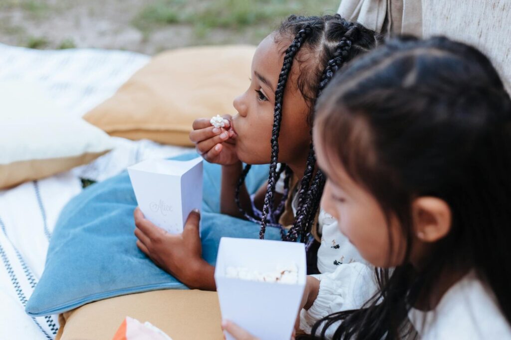 PTA fundraising ideas for elementary schools 2 Two girls relaxing outdoors, enjoying popcorn at a picnic, capturing a moment of leisure and childhood fun.
